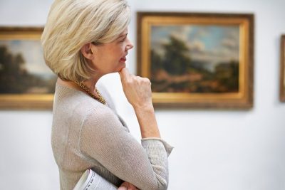 ""older white woman with hand to her chin observing art