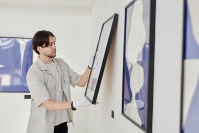 ""man hanging a framed artwork during exhibition install