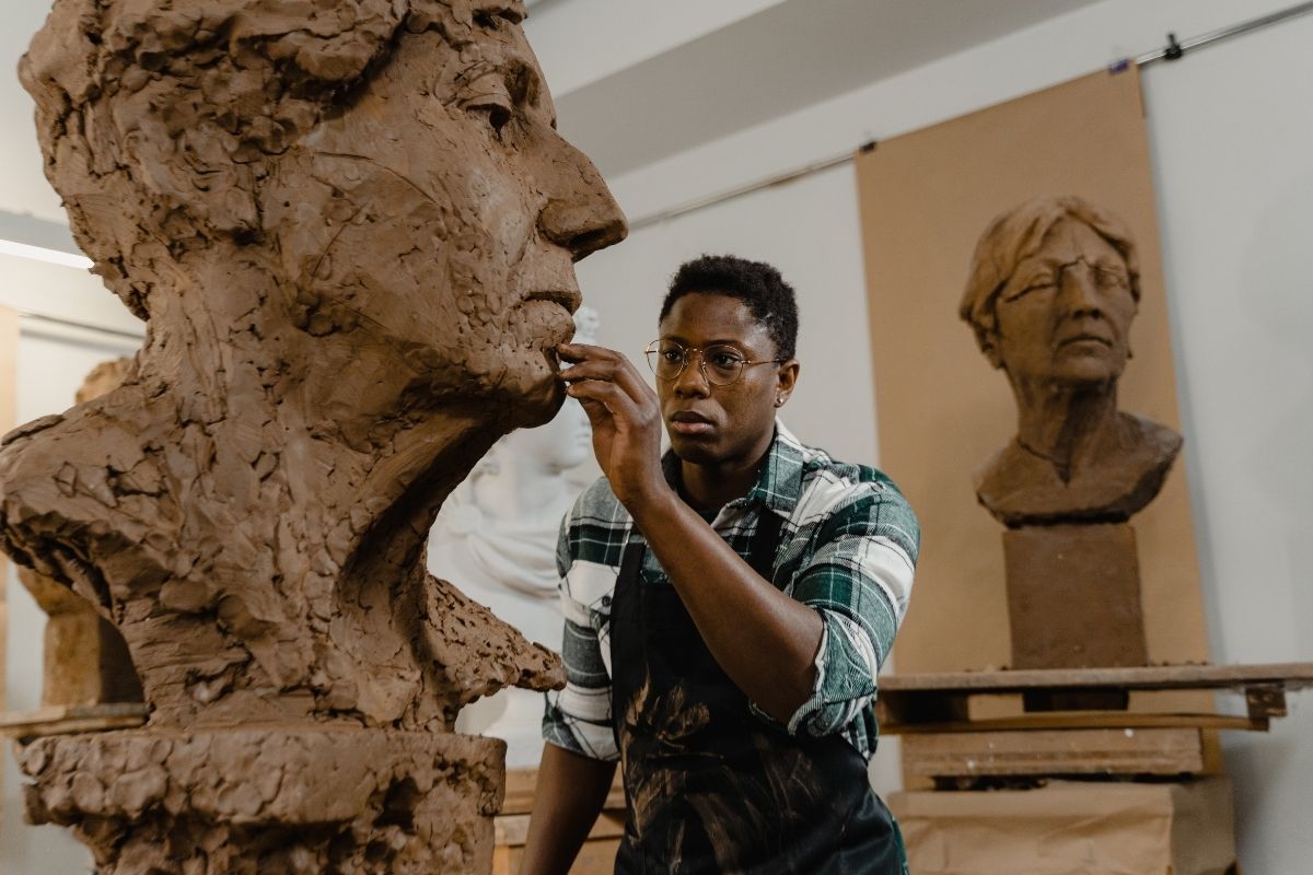 An artist sculpting the face of a clay bust in a studio
