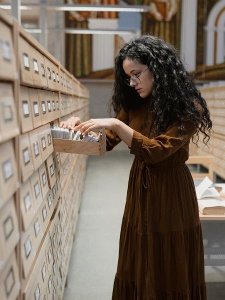 An archivist searching through a traditional card catalogue in a library archive, illustrating the collections management challenges TMS Collections is designed to address