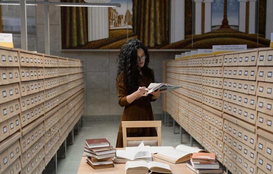 Collections staff reading in a room lined with card catalogue drawers, reflecting centralised archival records management