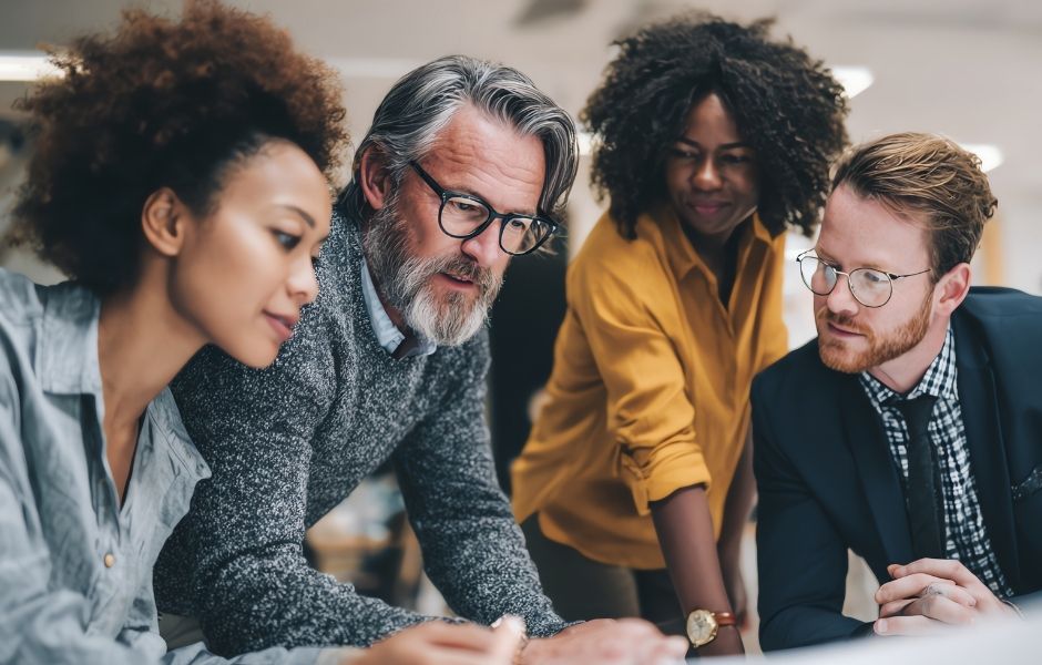 A diverse collections team in focused discussion, gathered closely around a shared workspace in a collaborative office environment