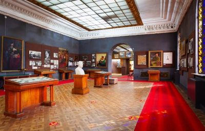 A formal military institution gallery with display cases, portraits, and a marble bust, representing collections requiring compliance and regulatory oversight