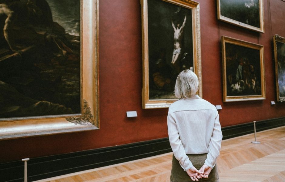 Preview of a TMS Collections downloadable brochure, depicting a visitor standing before large old master paintings on a deep red gallery wall