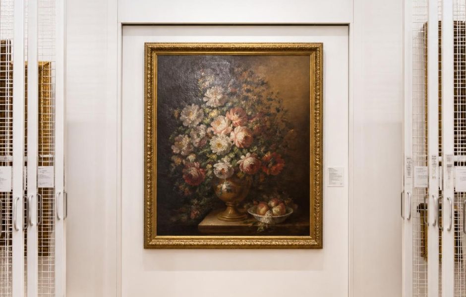 A framed painting on view within a secure collections storage area with sliding storage racks